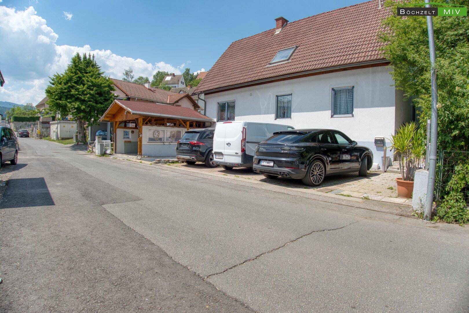 Straßenansicht des Einfamilienhauses mit Carport und mehreren geparkten Autos auf dem Grundstück.