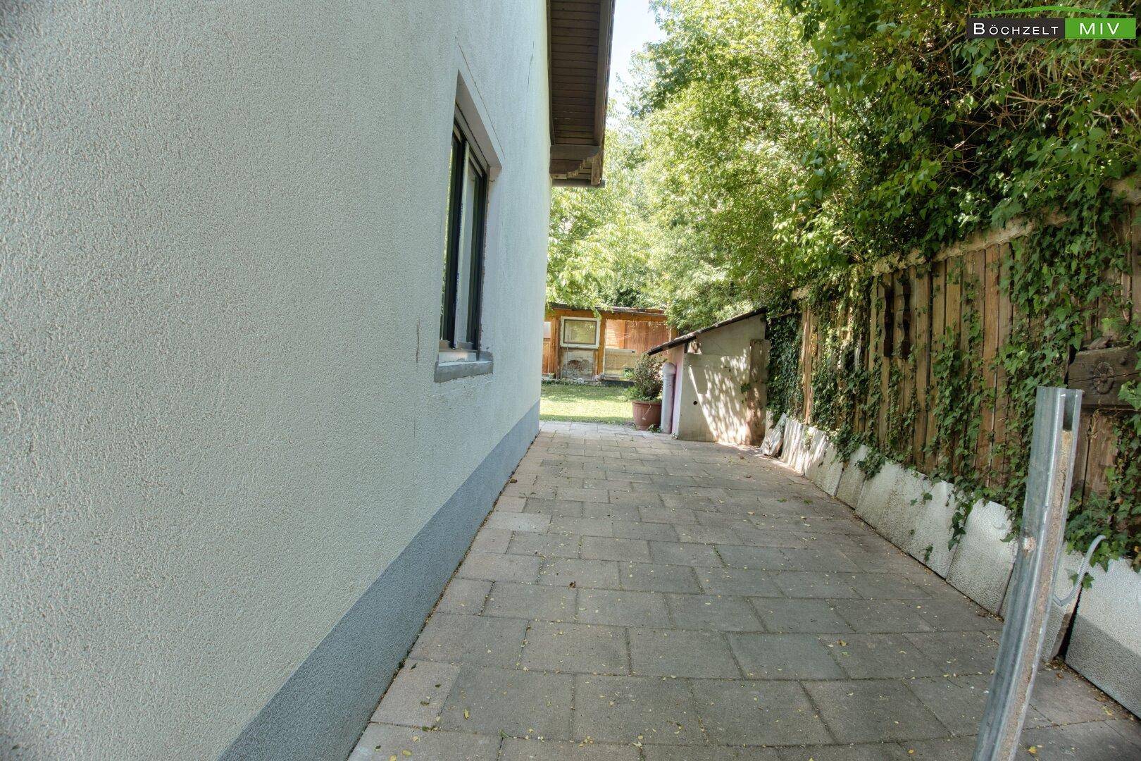 Gepflasterter Seitenweg entlang des Hauses, der zum hinteren Gartenbereich führt.