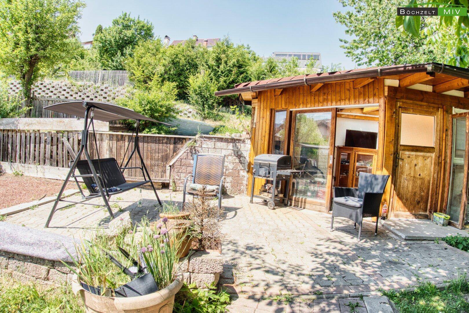 Gemütliche Terrasse mit Sitzgelegenheiten, Grill und einem kleinen Holzhaus im Garten.