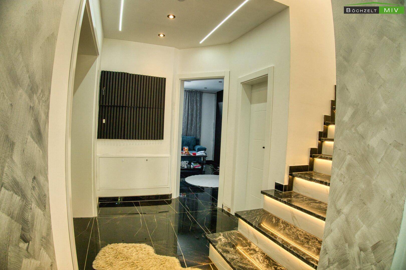 Moderner Eingangsbereich mit beleuchteter Marmortreppe und dunklem Fliesenboden.