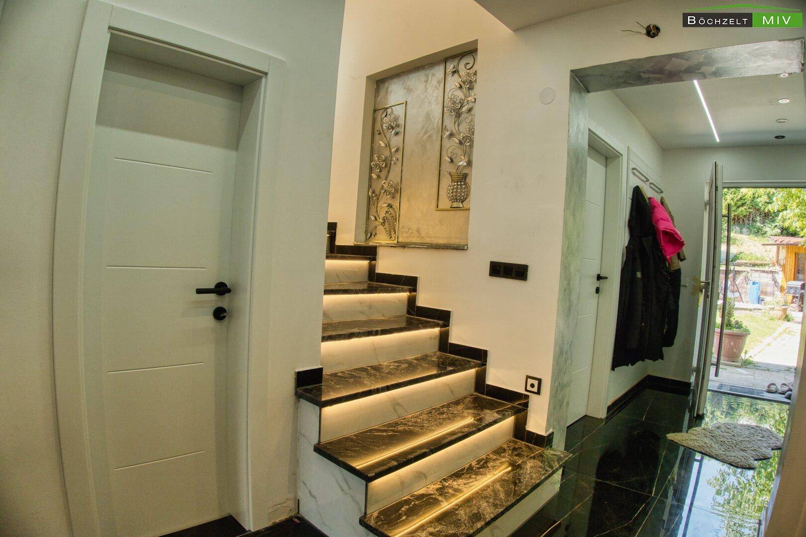 Heller Flur mit beleuchteter Marmortreppe und Zugang zum Außenbereich.