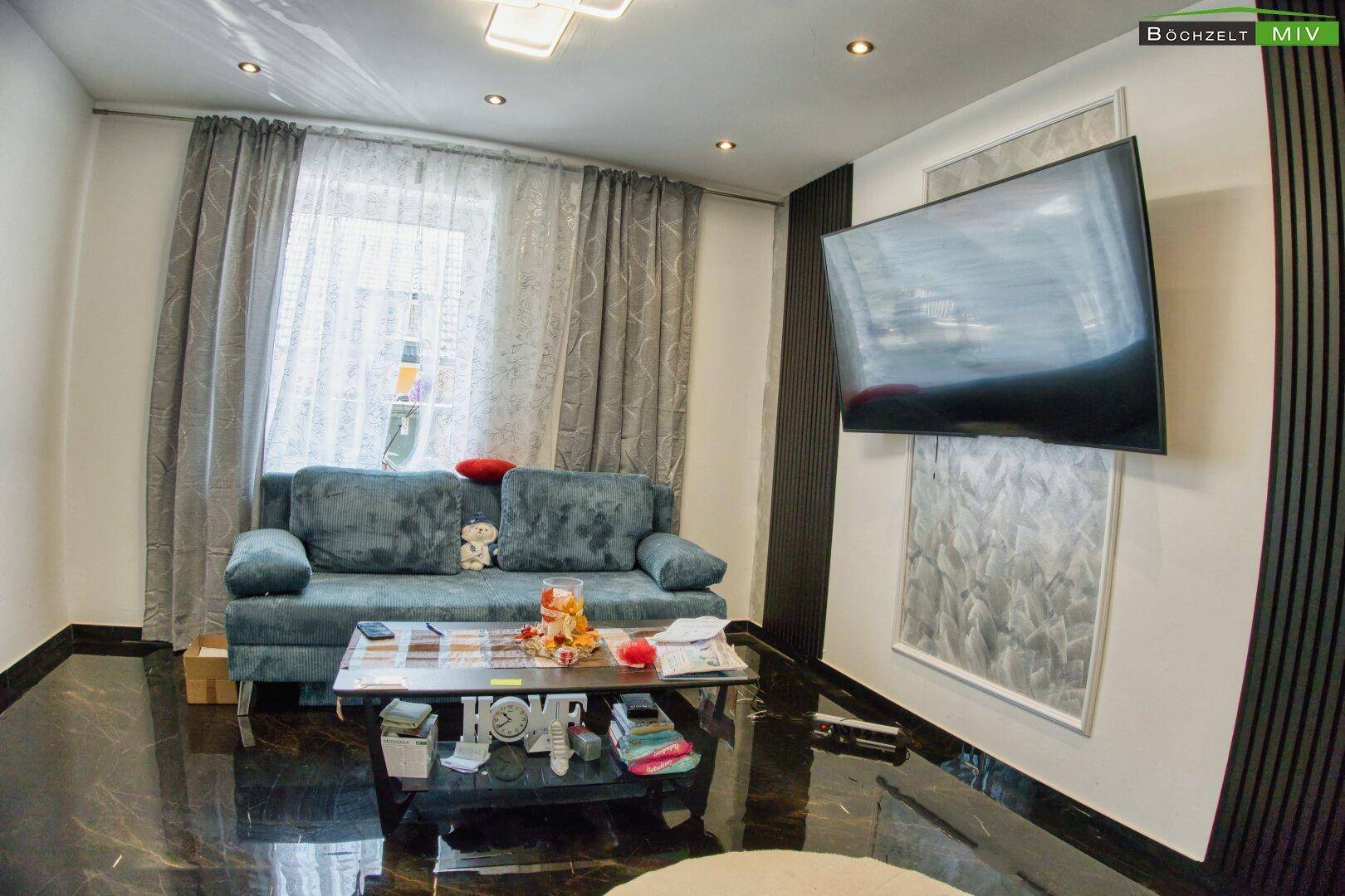 Wohnzimmer mit bequemer Couch, Couchtisch und großem Wandfernseher.