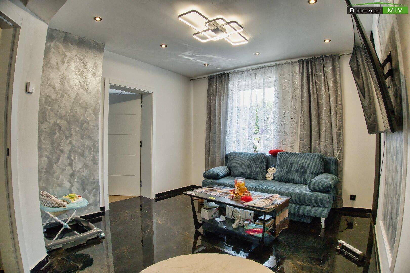 Helles Wohnzimmer mit moderner Einrichtung, dunklem Boden und Fenster.