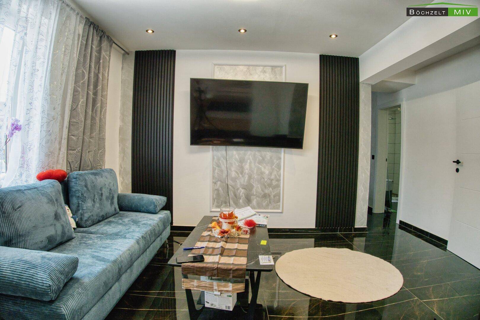 Modernes Wohnzimmer mit dunklem Boden, bequemer Couch und großem Fernseher.