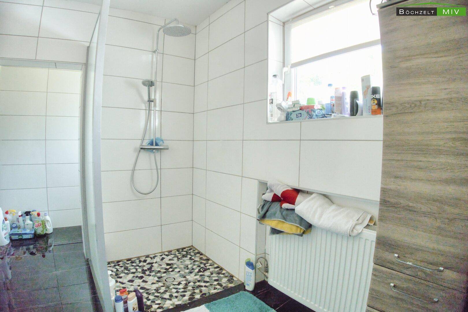 Badezimmer mit Duschbereich, weißen Fliesen und Fenster für Tageslicht.