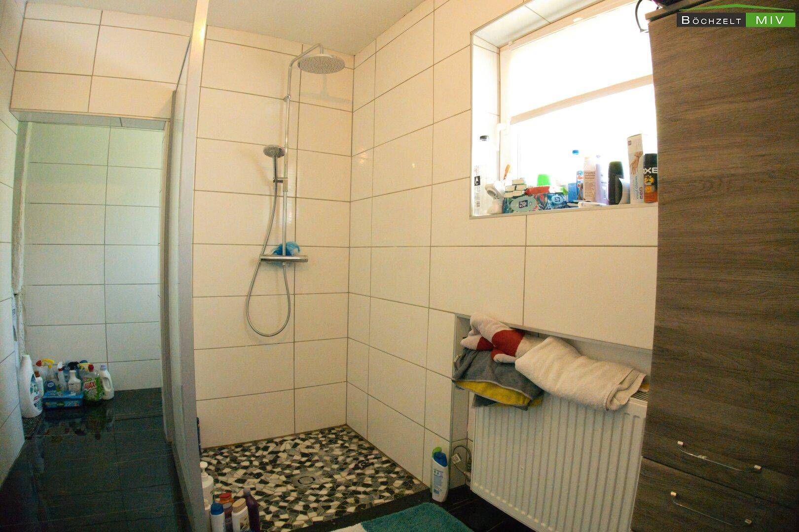 Helles Badezimmer mit Duschkabine, weißen Wandfliesen und Fenster.