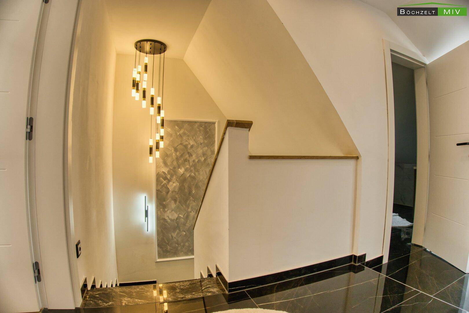 Treppenhaus von oben mit moderner Hängelampe und stilvoller Wandgestaltung.