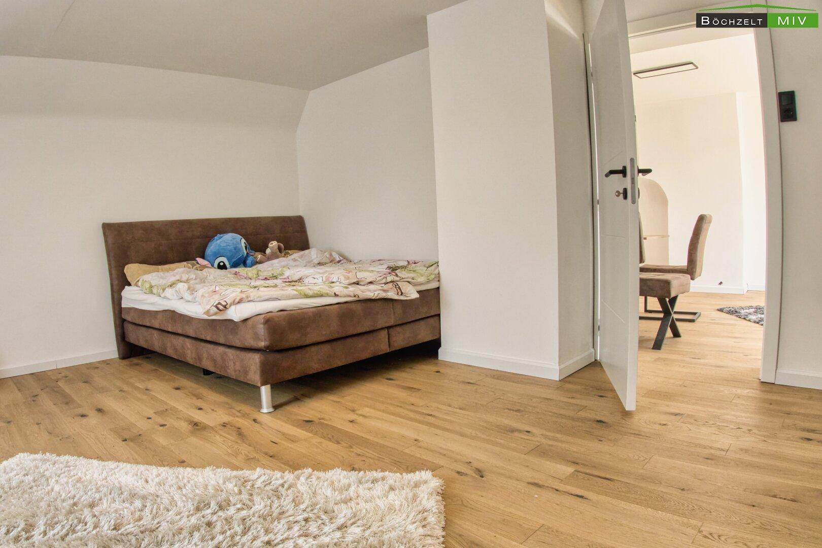 Schlafzimmer mit Holzboden und braunem Bett, offen zu einem weiteren Raum.