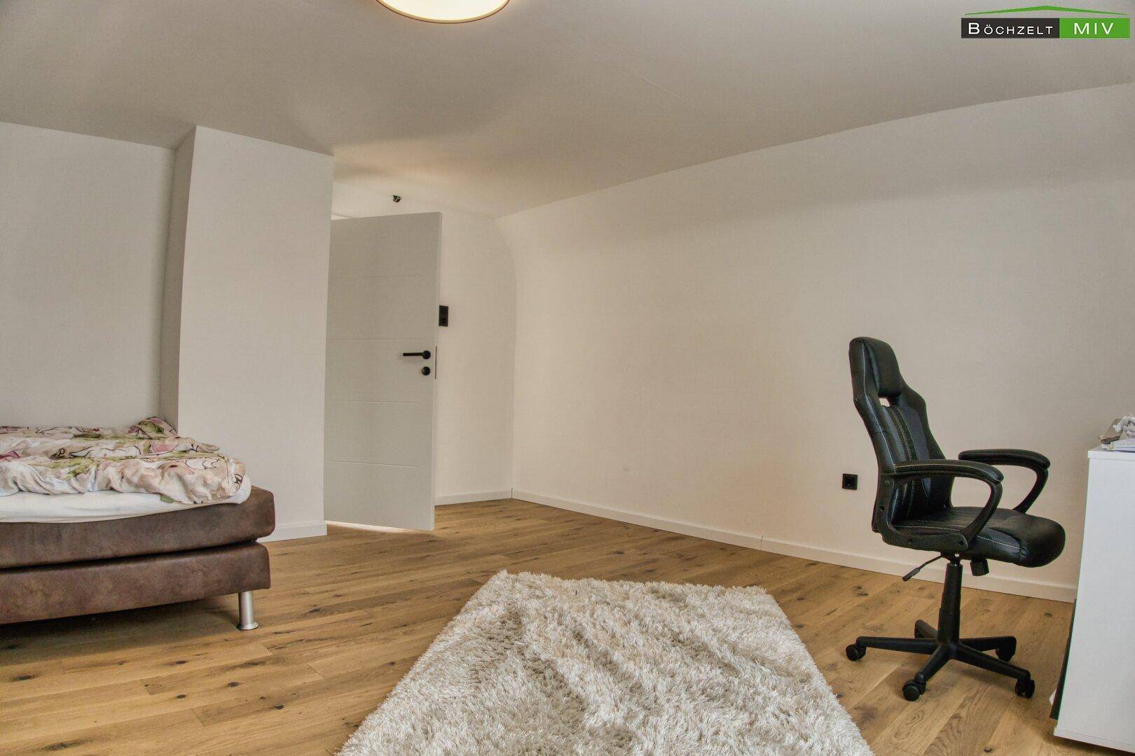 Schlafzimmer mit Holzboden, Bett und Schreibtisch, mit Zugang zu einem anderen Raum.