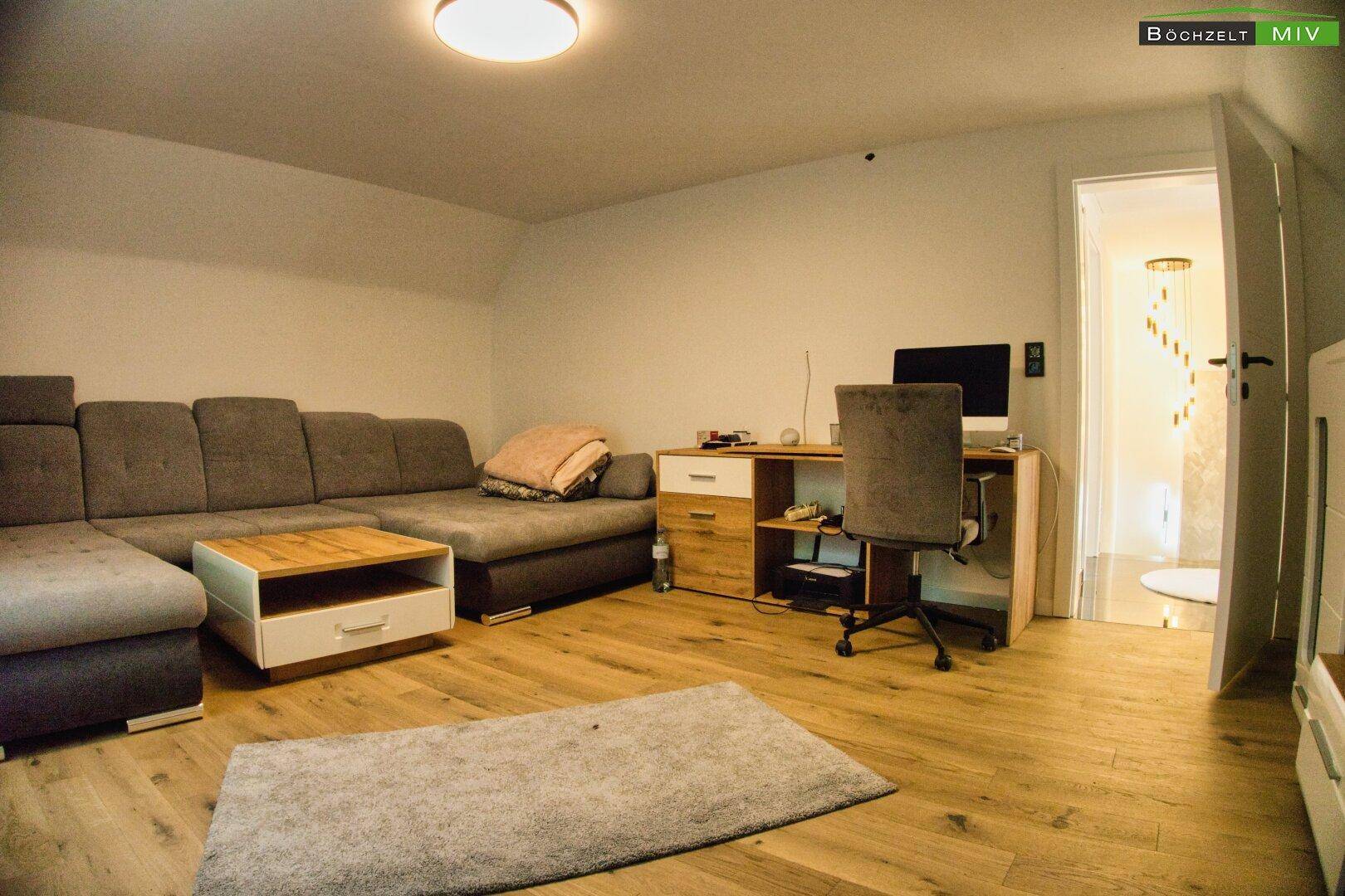 Gemütliches Wohnzimmer mit Ecksofa, Holzboden und Arbeitsbereich, offen zum Flur.