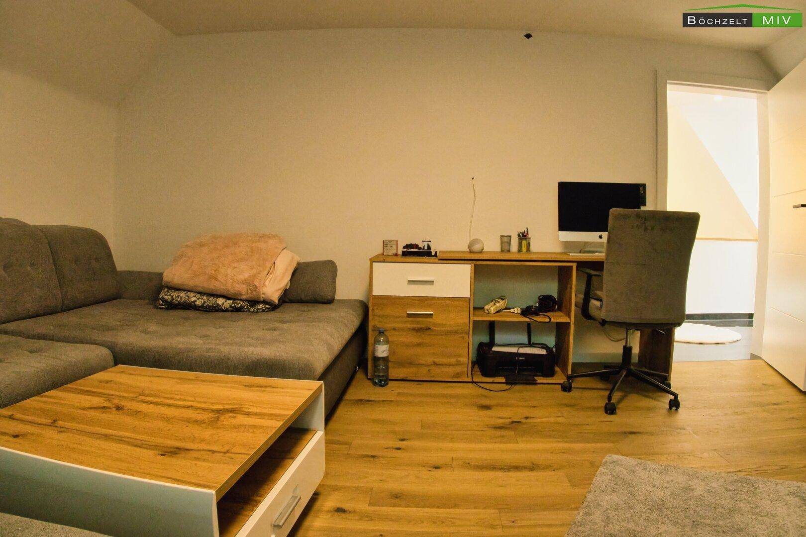 Wohnzimmer mit Ecksofa, Couchtisch und Arbeitsplatz, eingerichtet für Komfort.