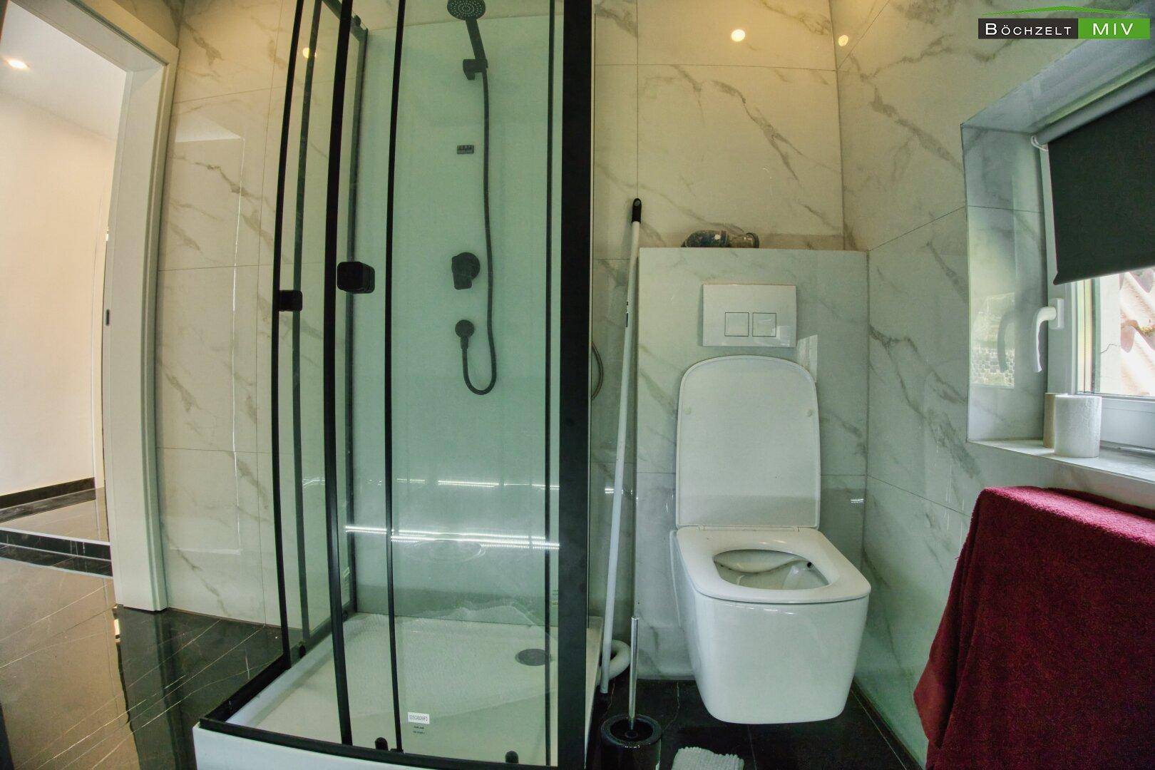Helles Badezimmer mit Duschkabine, Wand-WC und Fenster, ausgestattet mit modernen Fliesen.
