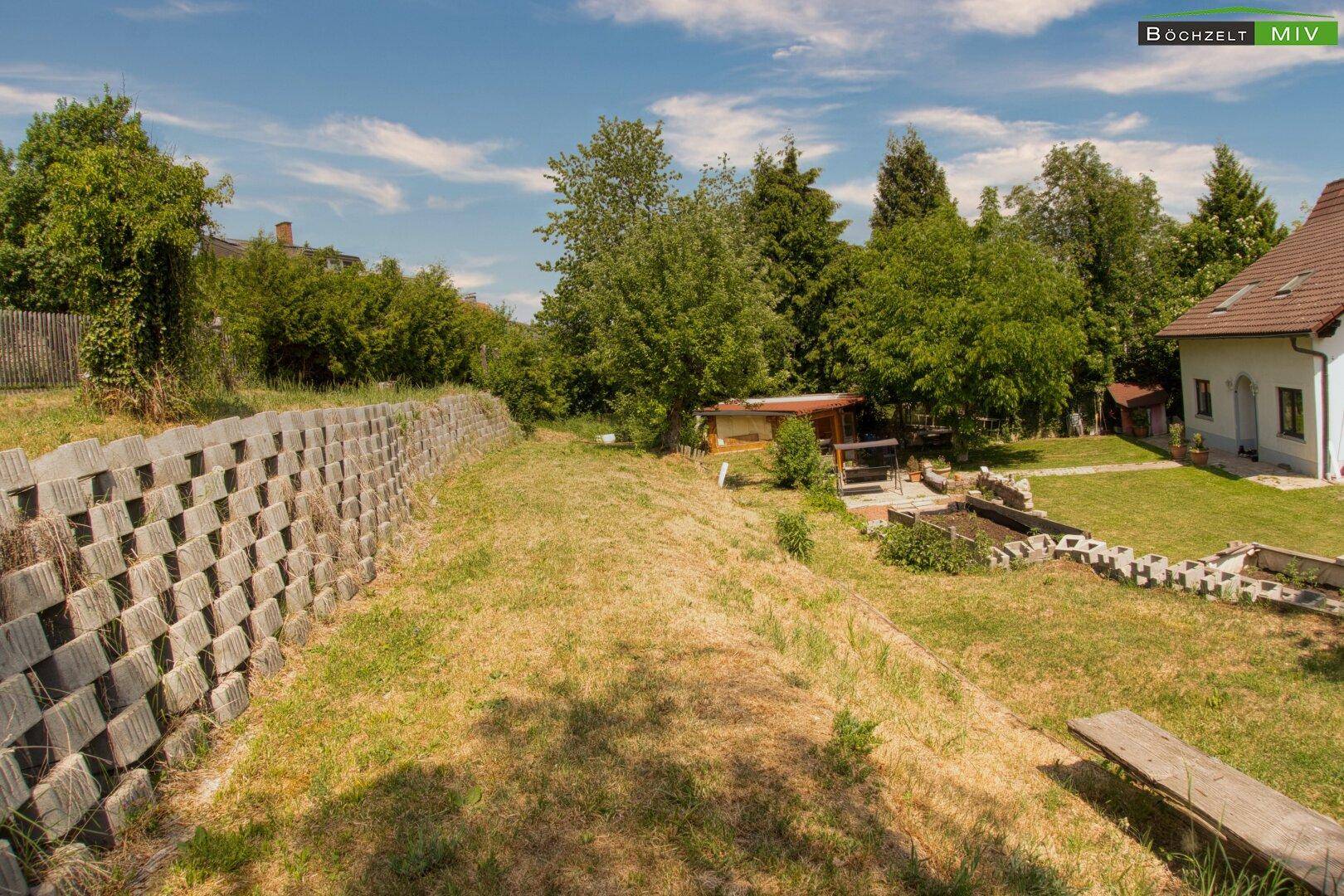 Weitläufiger Garten mit Rasen, Bäumen und einer Stützmauer, ideal für Erholung.