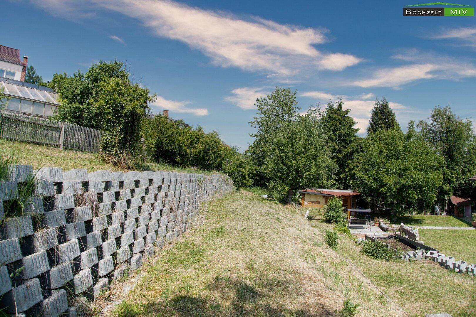 Abfallender Gartenbereich mit Stützmauer und viel Grün, bietet Potenzial zur Gestaltung.