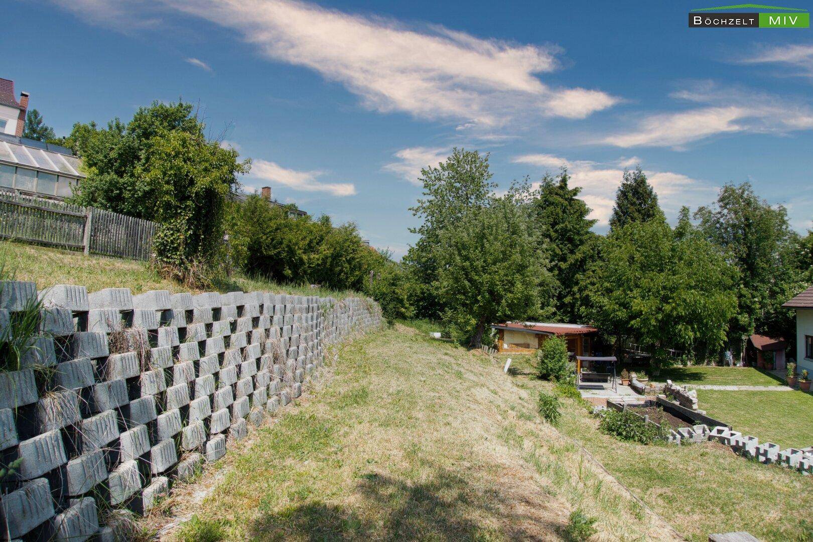 Abfallender Gartenbereich mit Stützmauer und viel Grün, bietet Potenzial zur Gestaltung.