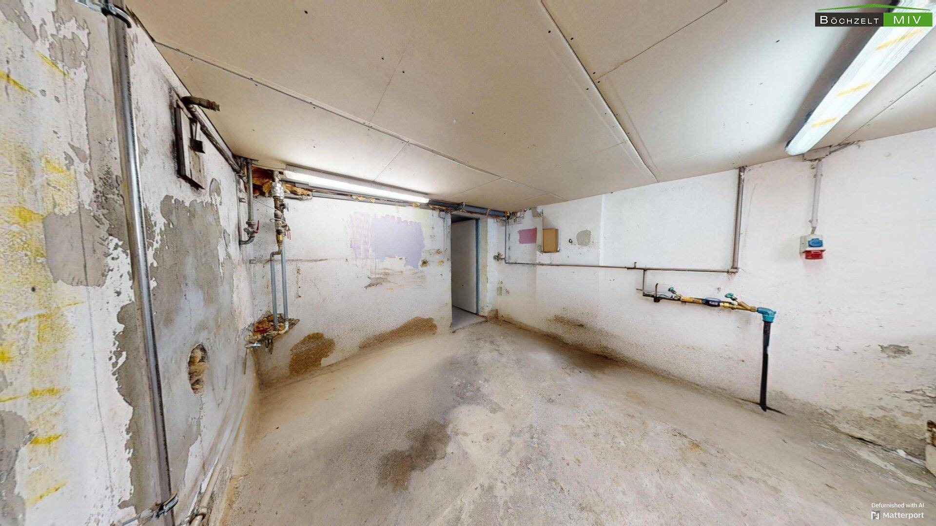 Kellerraum mit Betonboden, sichtbaren Installationen und Renovierungsbedarf.