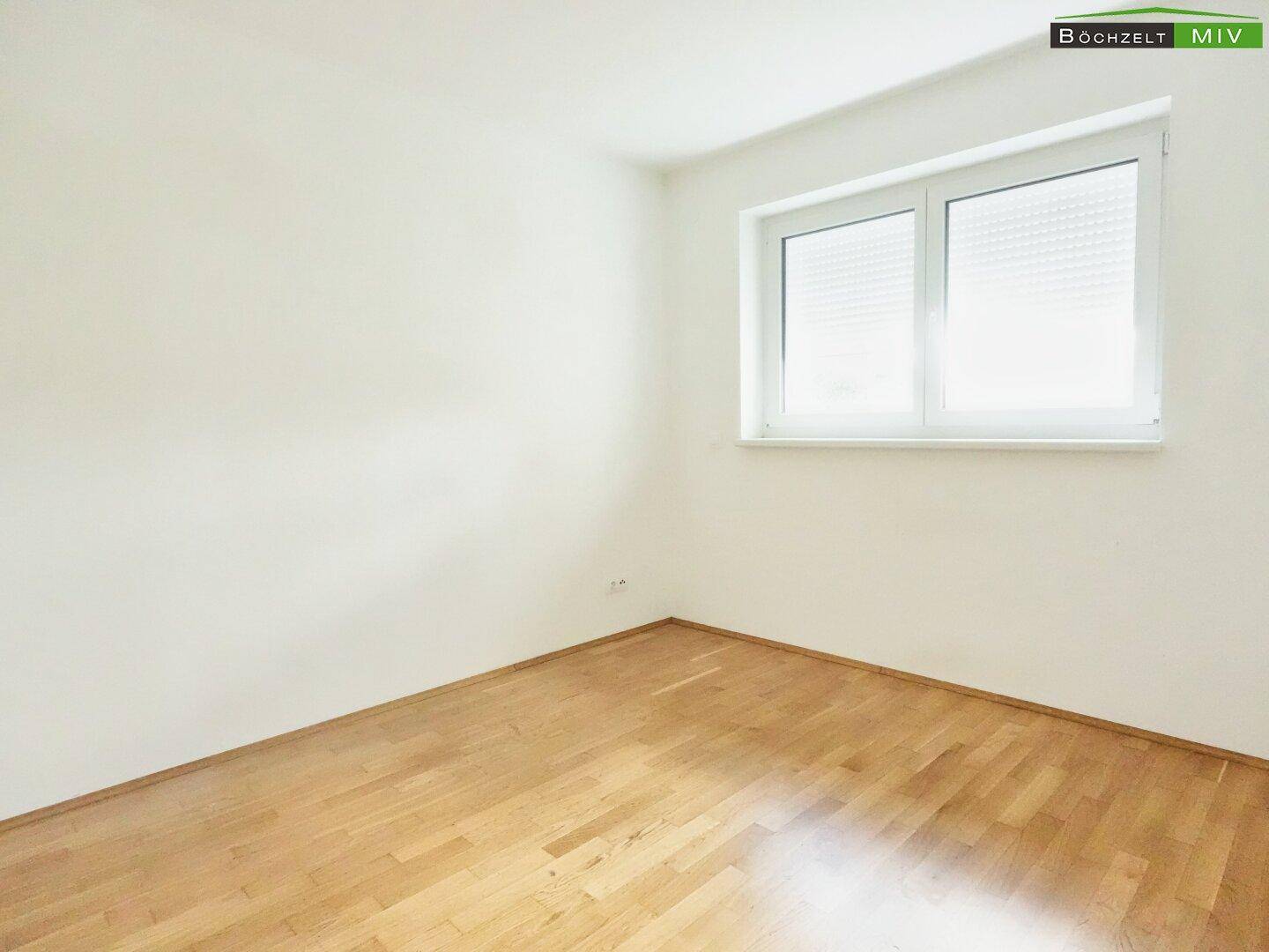 Helles Zimmer mit Parkettboden und Fenster mit Rollladen, ideal als Schlaf- oder Arbeitszimmer.