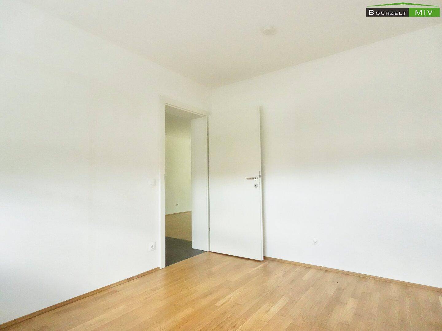 Leeres Zimmer mit Parkettboden und weißer Tür, bereit für individuelle Gestaltung.