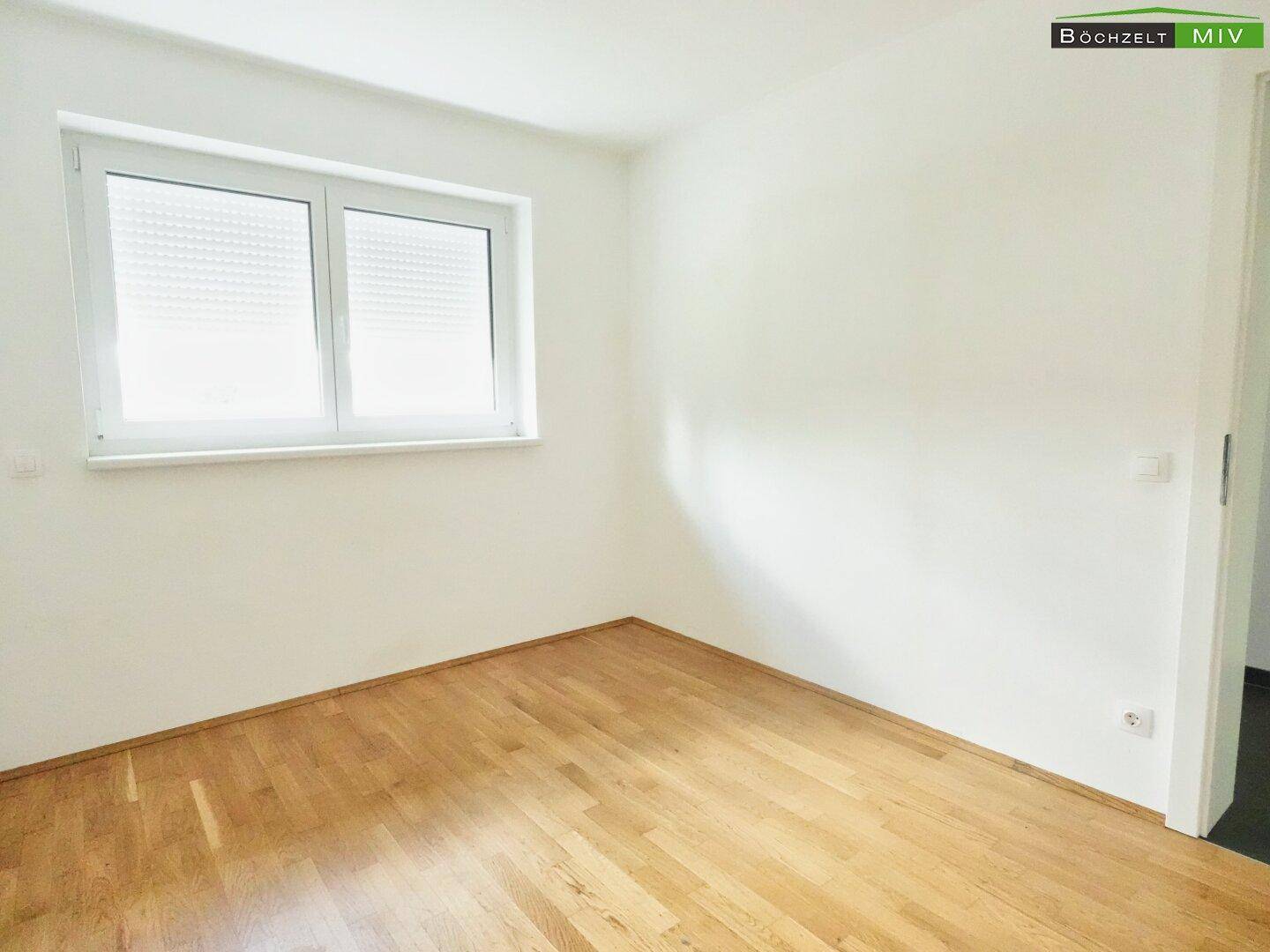 Helles Zimmer mit Parkettboden und Fenster mit Rollladen, bietet viel Tageslicht.