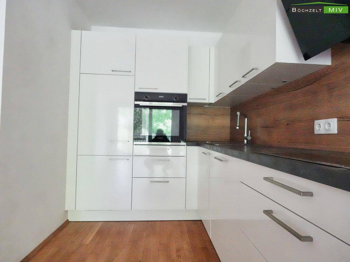 Moderne Einbauküche mit weißen Fronten, integriertem Backofen und Holzakzenten.