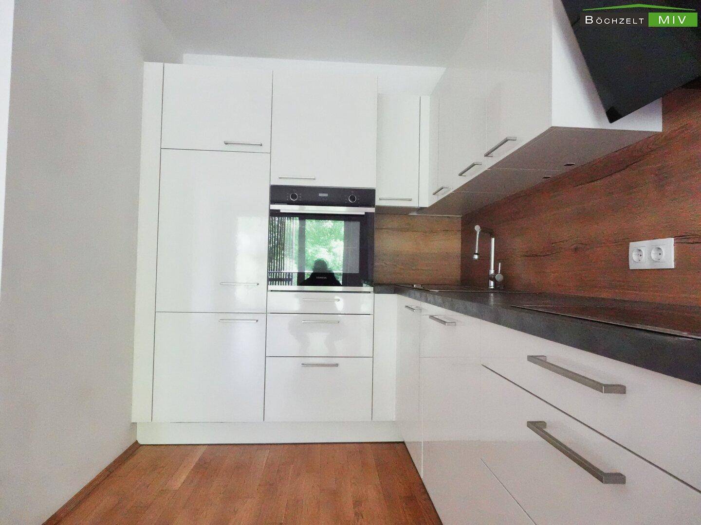 Moderne Einbauküche mit weißen Fronten, integriertem Backofen und Holzakzenten.