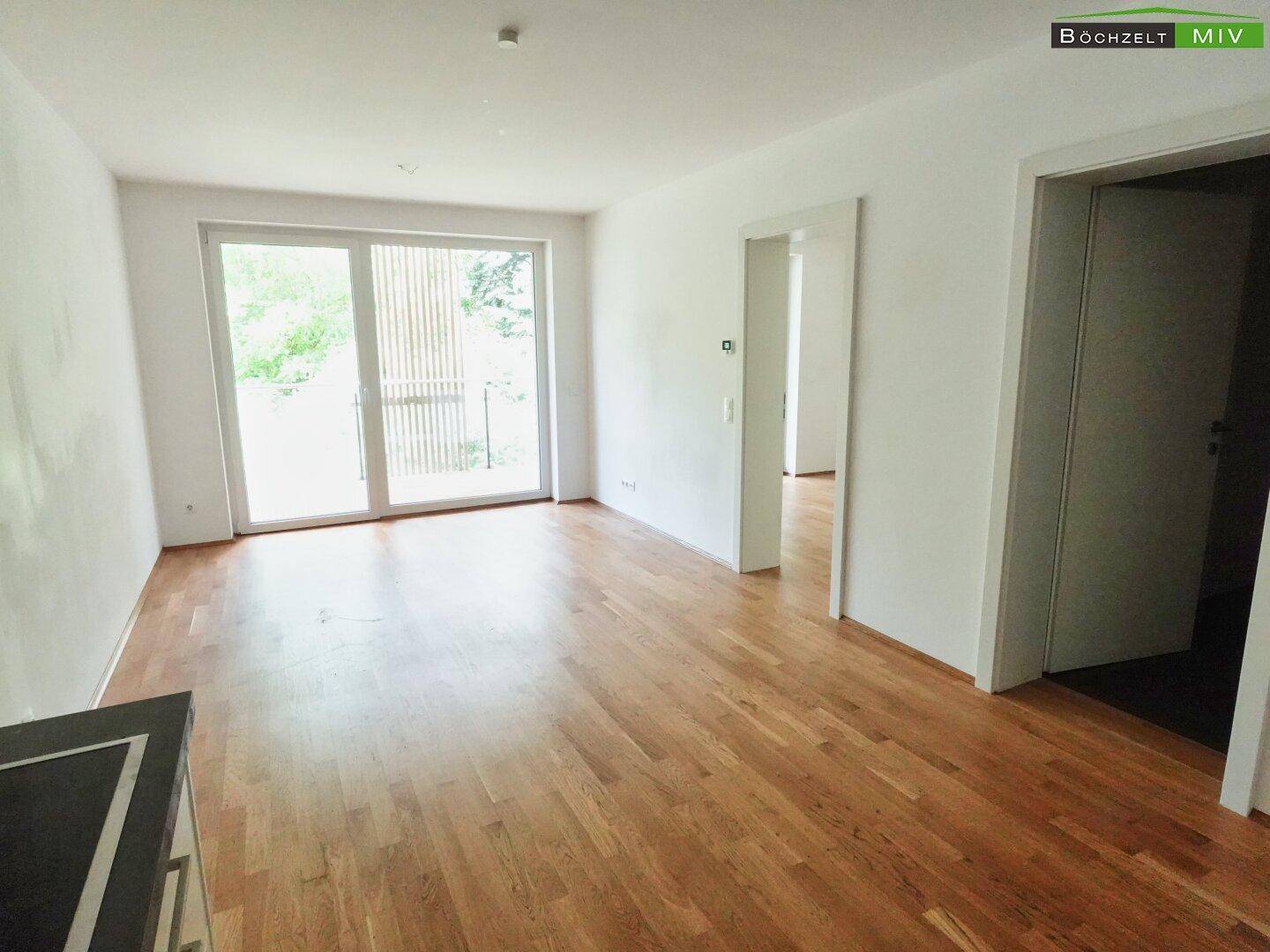 Heller Wohnbereich mit Parkettboden und Zugang zu einem Balkon, bietet viel Tageslicht.