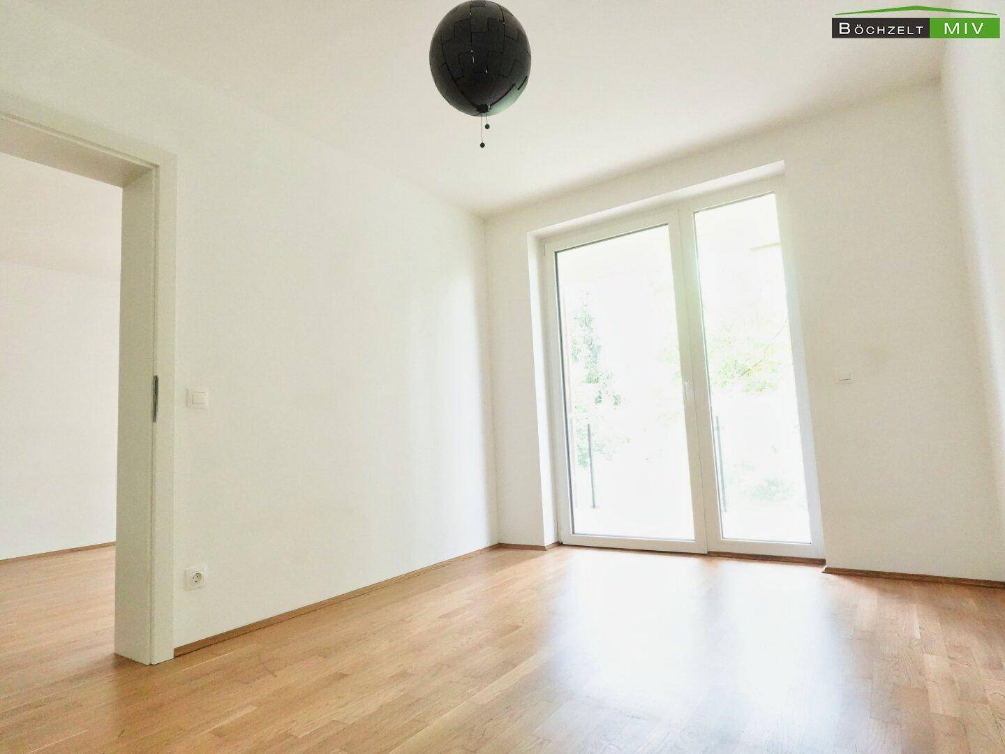 Helles Zimmer mit Parkettboden und großer Balkontür, die viel Licht hereinlässt.
