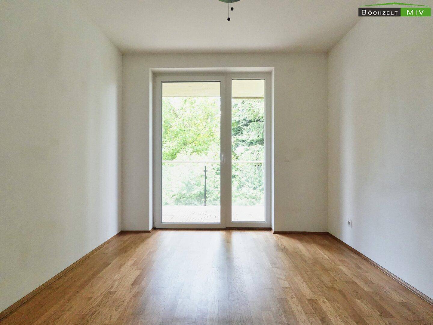 Helles Zimmer mit Parkettboden und großer Balkontür, bietet einen Blick ins Grüne.