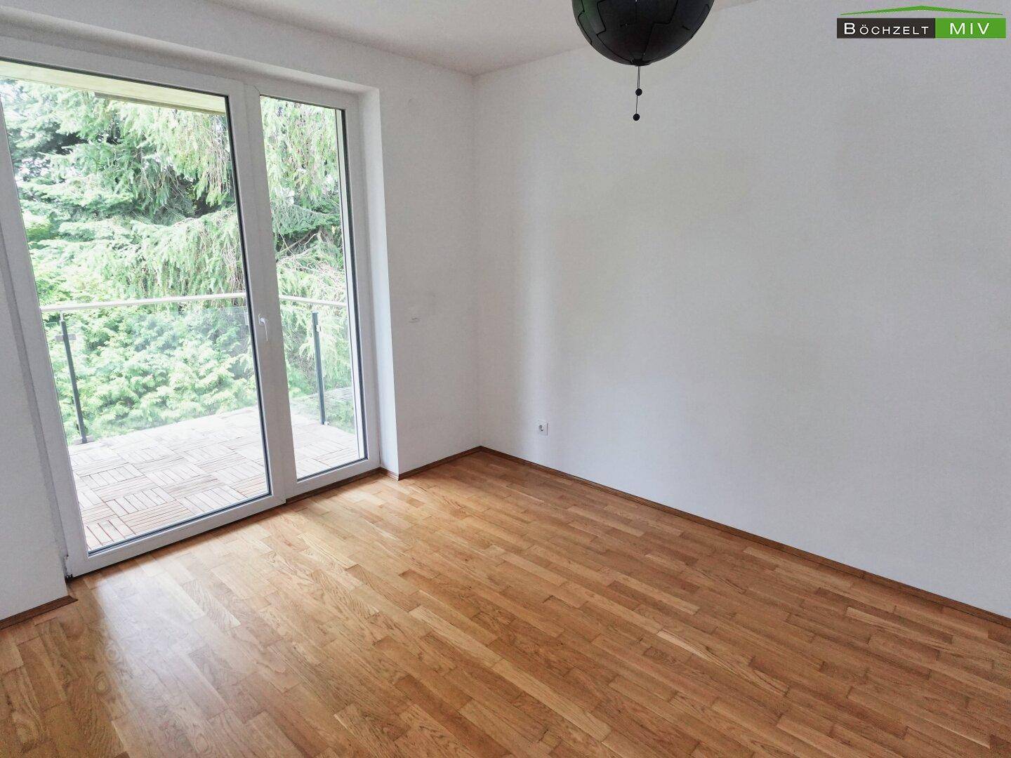 Helles Zimmer mit Parkettboden und großer Balkontür, die viel Licht hereinlässt.