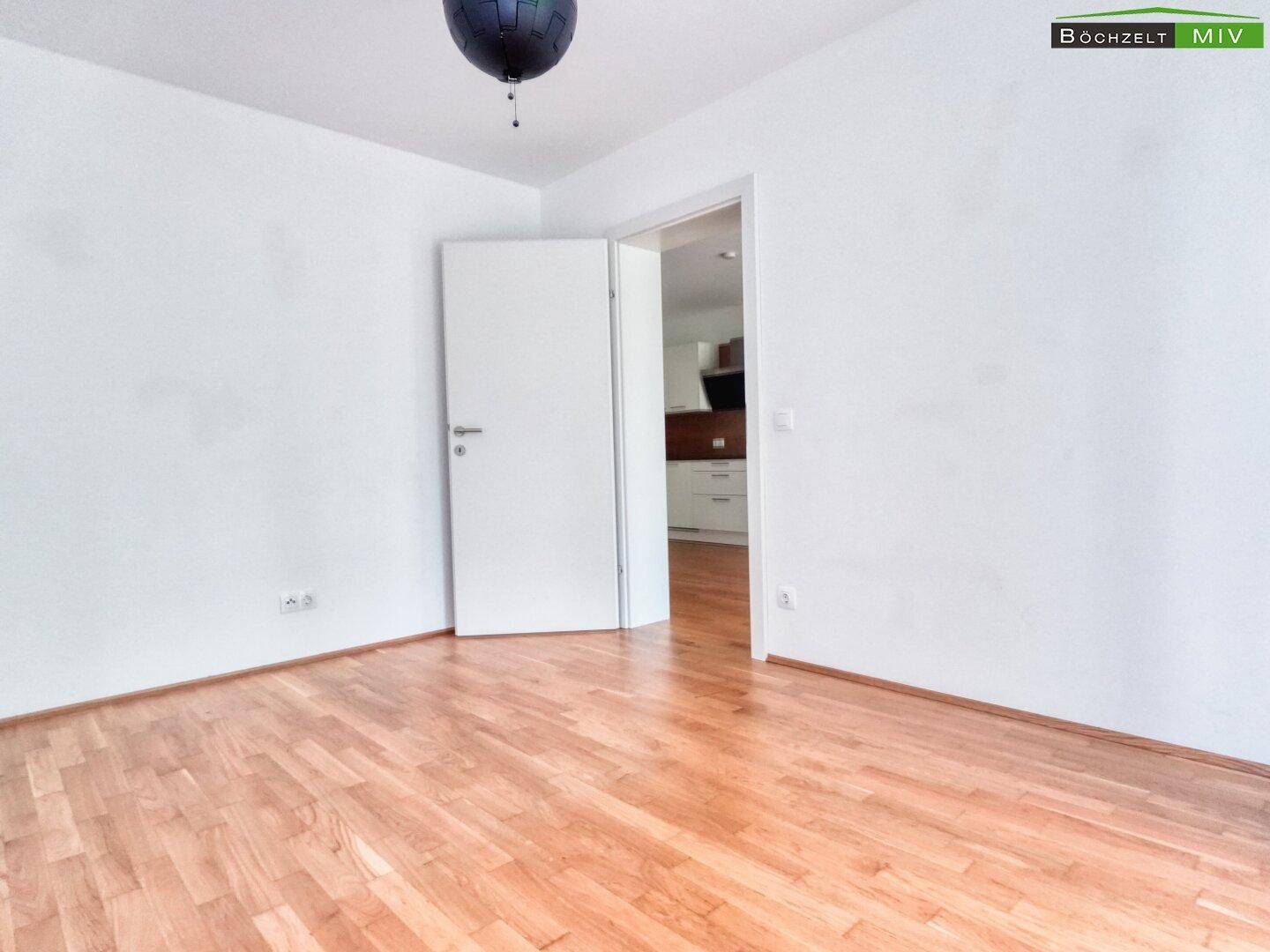 Helles Zimmer mit Parkettboden und weißer Tür, mit Blick auf die moderne Küche.