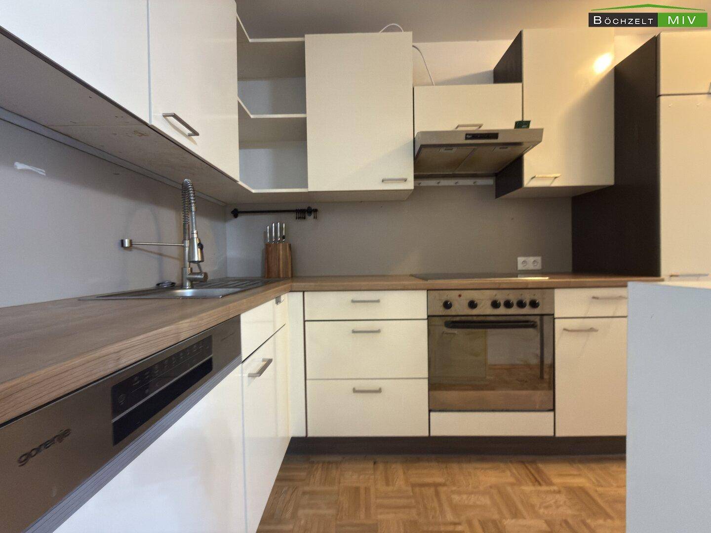 Funktionale Einbauküche mit weißen Schränken, Holz-Arbeitsplatte und integriertem Geschirrspüler.