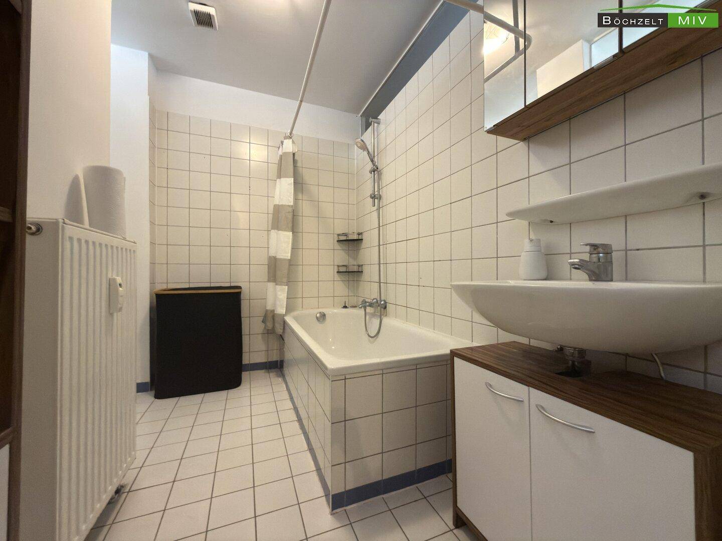 Gefliestes Badezimmer mit Badewanne, Waschbecken und Holzunterschrank.