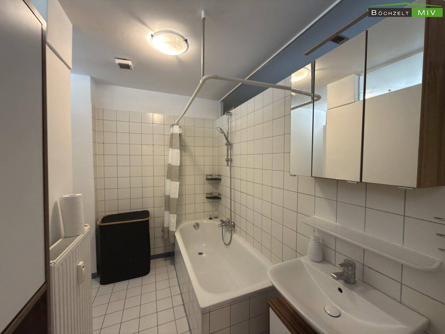 Gefliestes Badezimmer mit Badewanne, Waschbecken und Spiegelschrank.