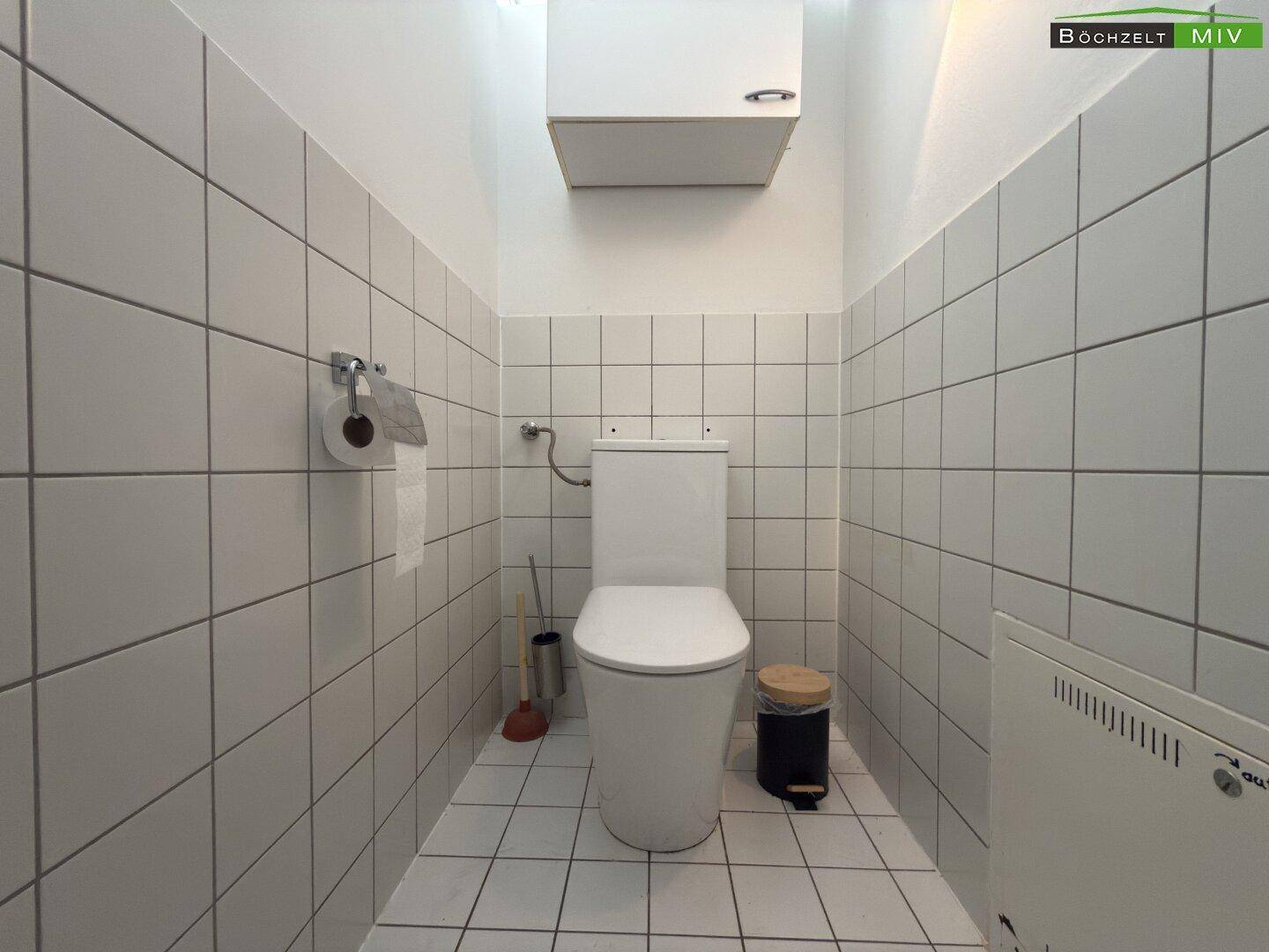 Separate Toilette mit weißen Fliesen und wandmontiertem WC.
