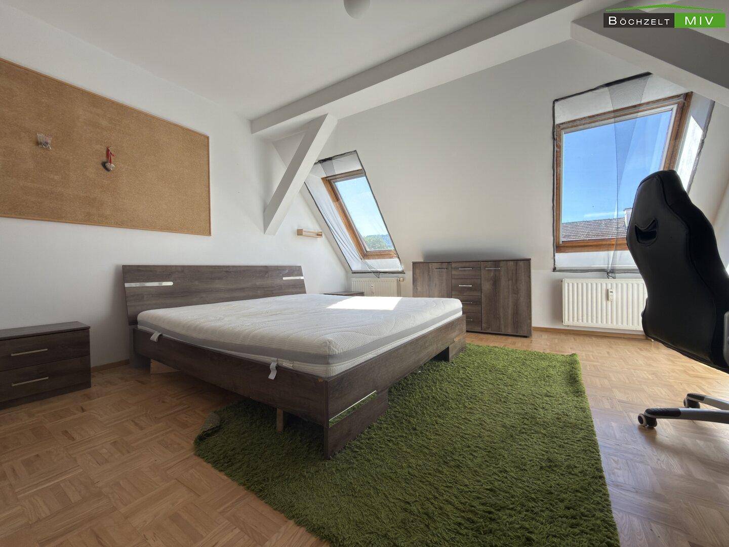 Schlafzimmer mit Holzbett, Parkettboden und zwei Dachfenstern.