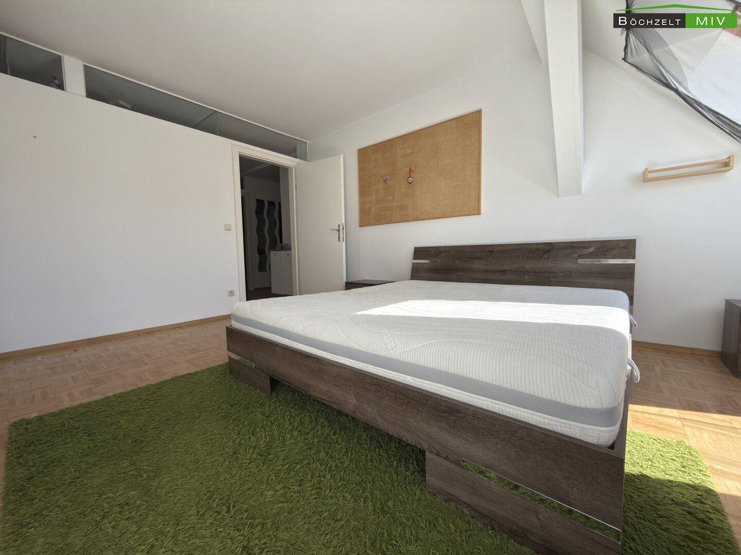 Schlafzimmer im Dachgeschoss mit Holzbett, grünem Teppich und Parkettboden.
