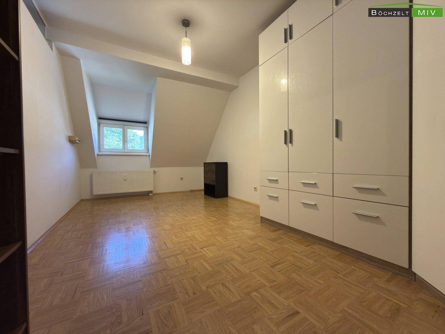 Geräumiges Schlafzimmer mit Parkettboden, Einbauschrank und Dachschräge.