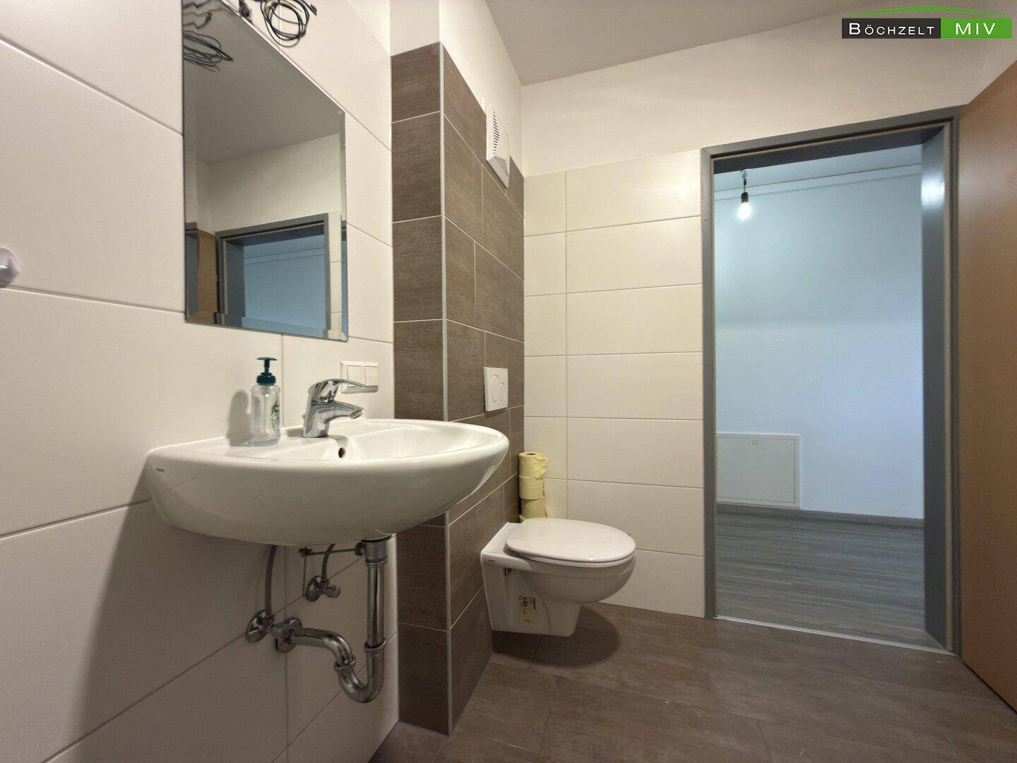 Helles Badezimmer mit modernem Waschbecken, wandhängendem WC und einer Kombination aus weißen und braunen Fliesen.
