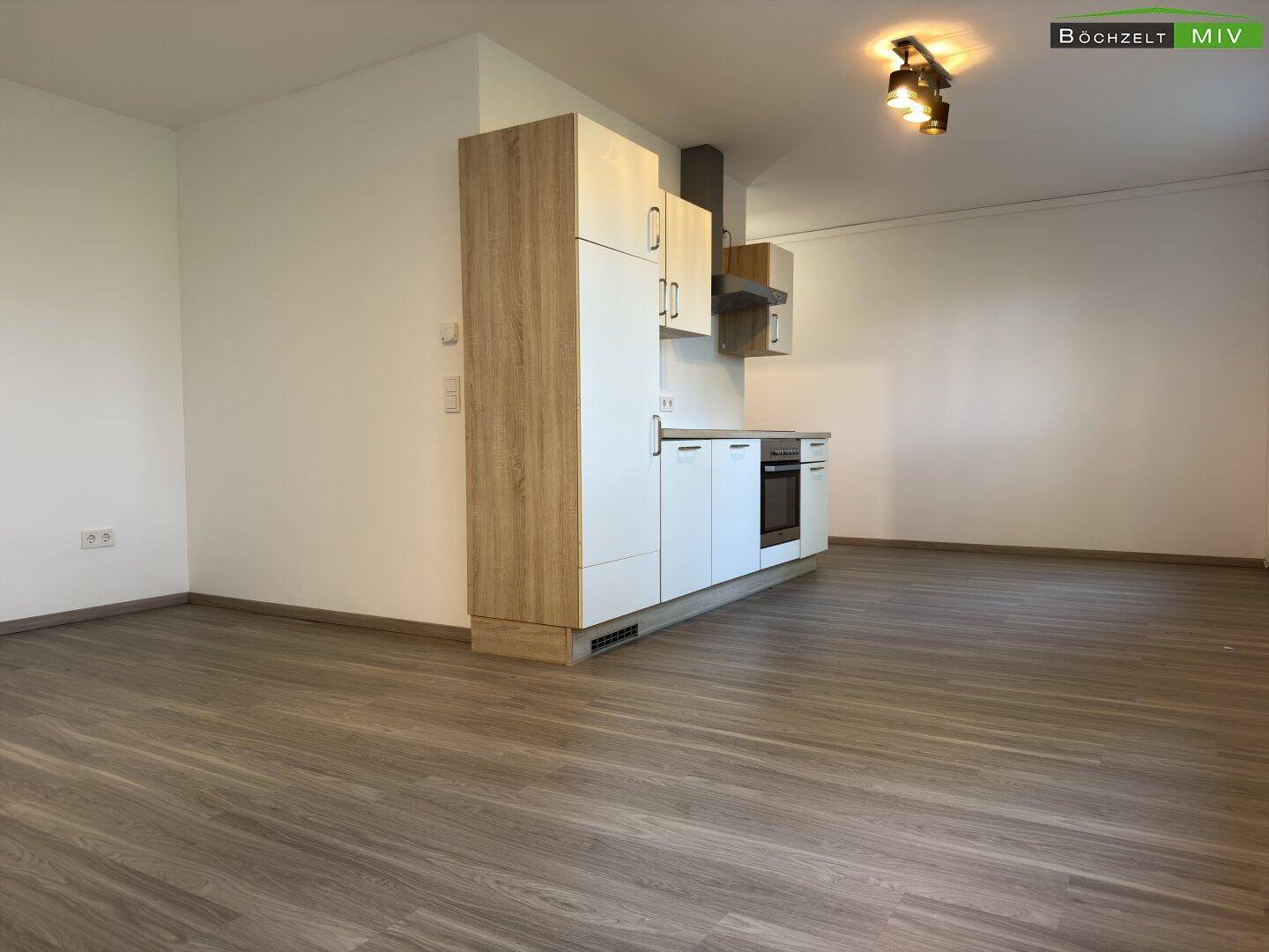 Offener Wohnbereich mit einer kompakten Küchenzeile, hellem Laminatboden und viel Platz für individuelle Gestaltung.