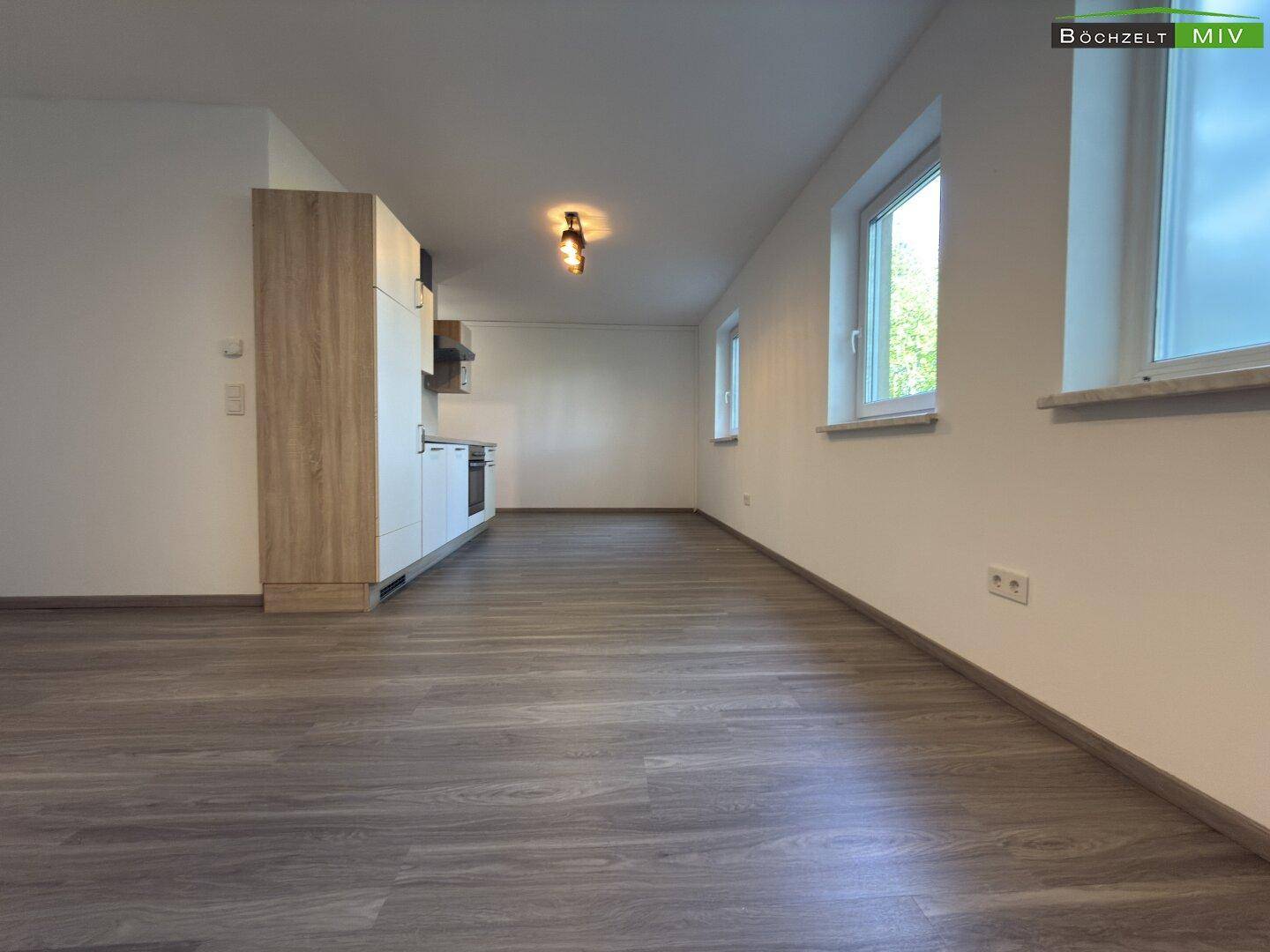 Langer, heller Wohnbereich mit teilweiser Küchenzeile, Laminatboden und Fenstern, die viel Licht hereinlassen.