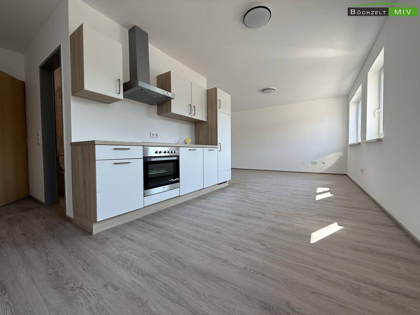 Offener Raum mit moderner Küchenzeile, Laminatboden und viel Tageslicht durch die Fenster.