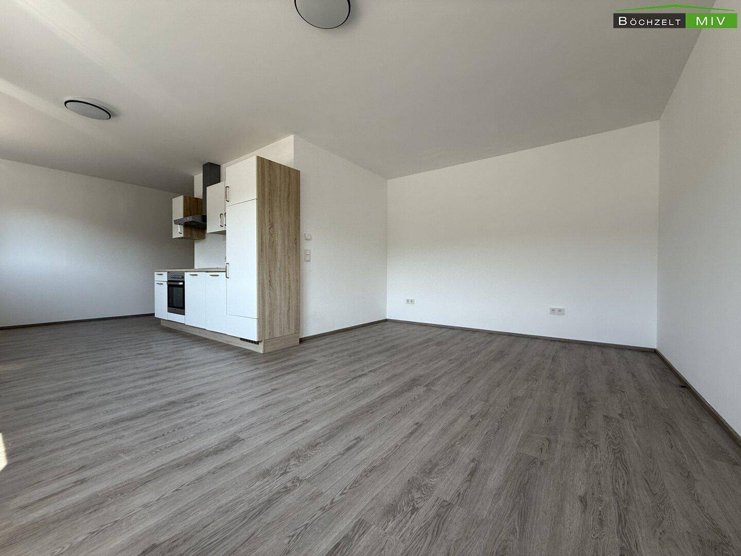 Geräumiger, offener Bereich mit integrierter Küchenzeile und hellem Laminatboden, ideal für flexible Nutzung.