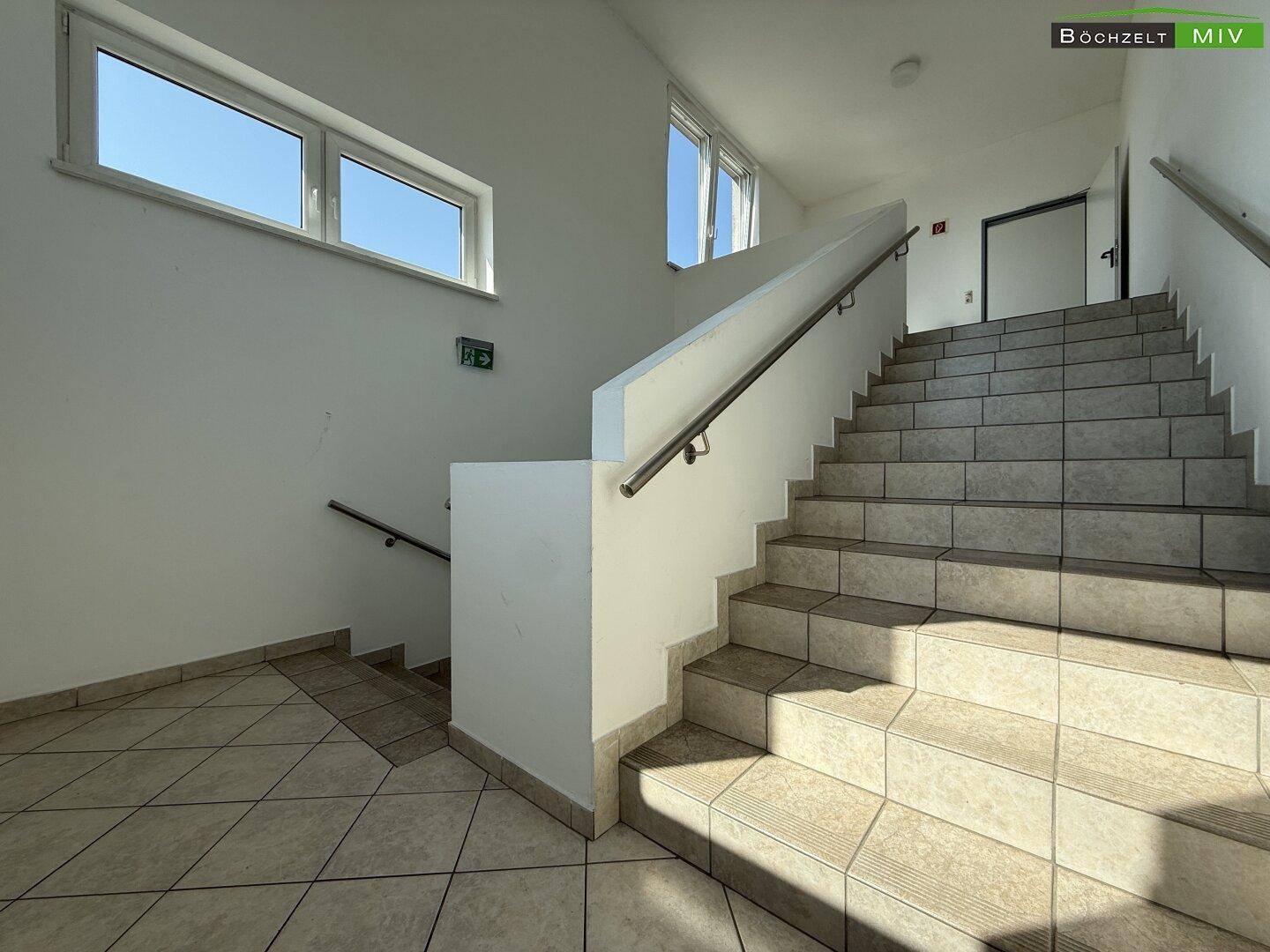 Helles Treppenhaus mit Fliesenboden und Fenstern, die viel Tageslicht hereinlassen und eine offene Atmosphäre schaffen.