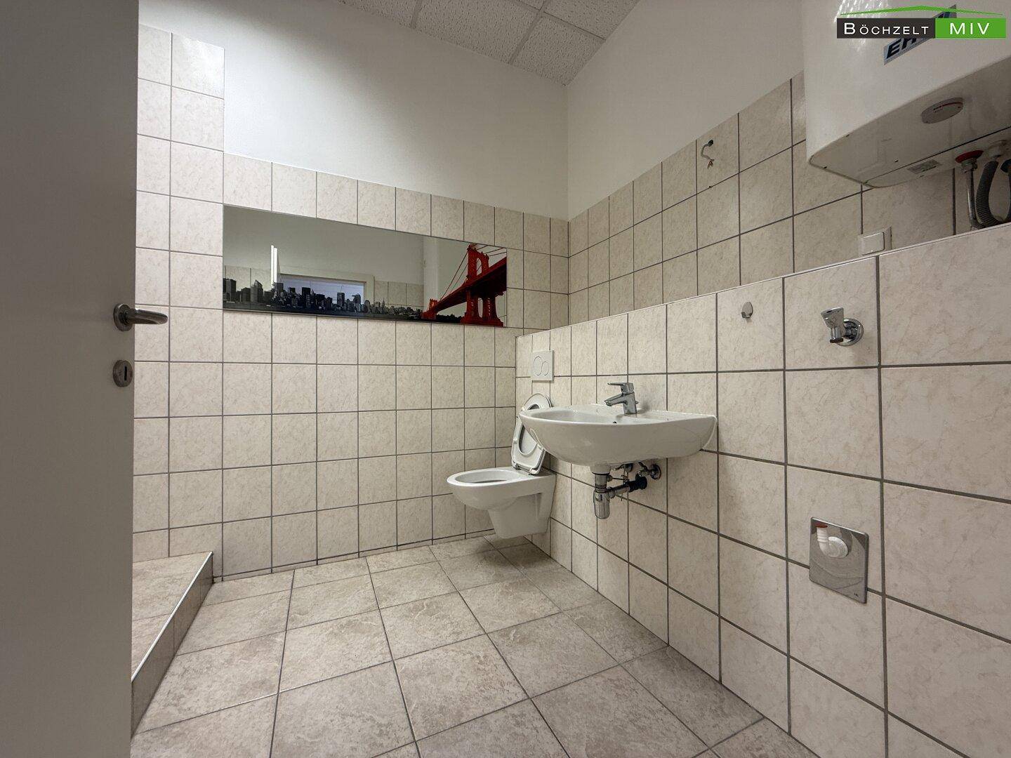 Gefliestes Badezimmer mit WC, Waschbecken und einem Spiegel, der eine Stadtansicht reflektiert.