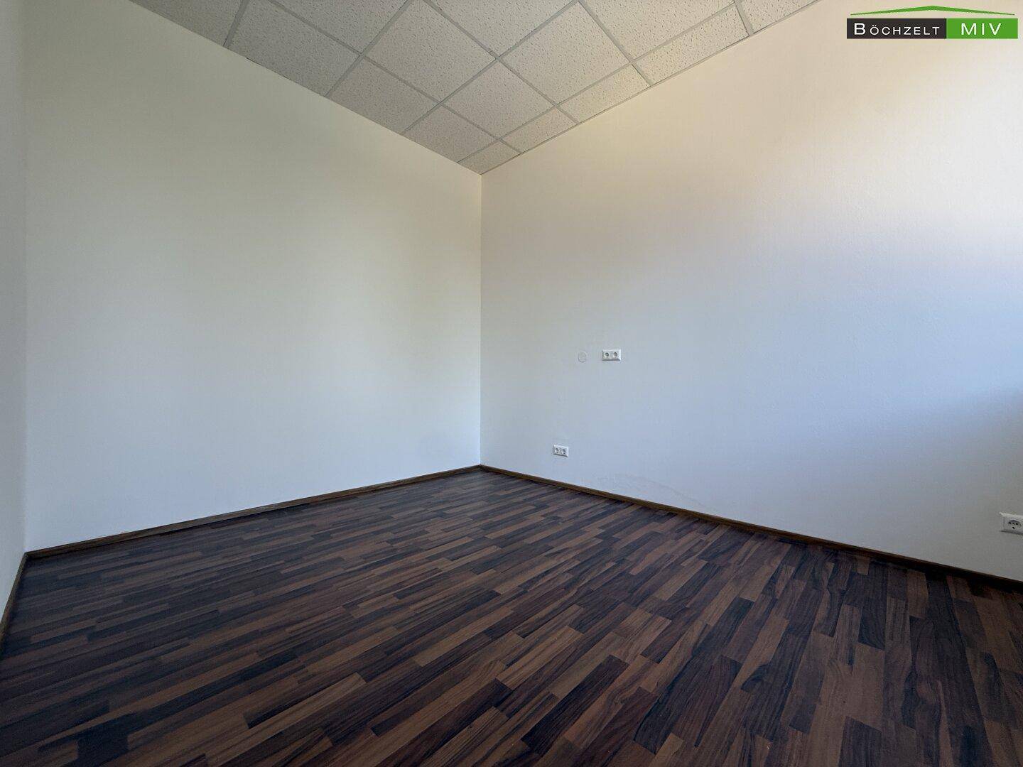 Heller, leerer Raum mit dunklem Laminatboden und einer abgehängten Decke, bereit zur individuellen Gestaltung.