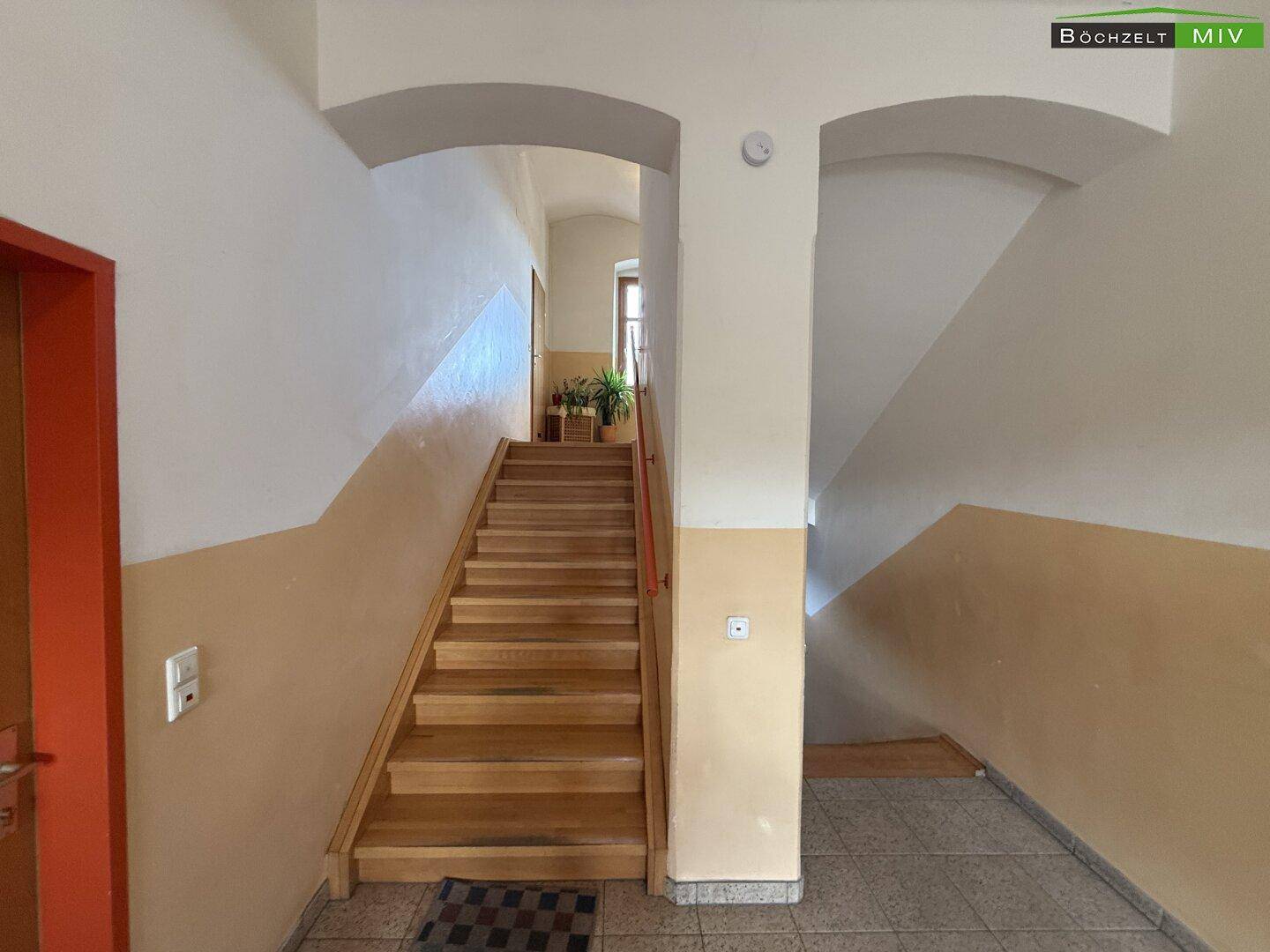 Treppenhaus mit Holzstufen und weiß-beigen Wänden, das zu den oberen Etagen führt.