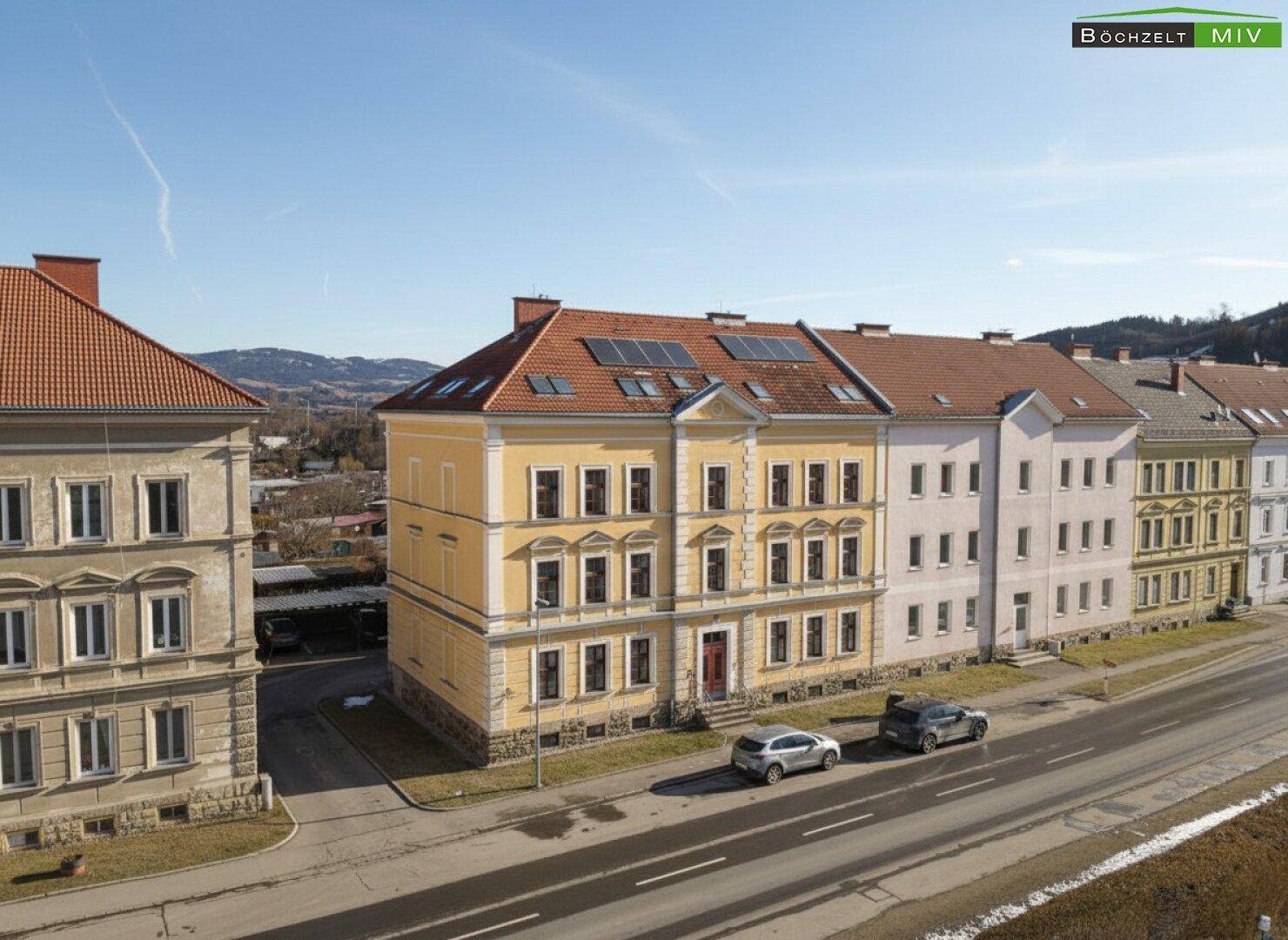 Seitenansicht eines historischen Gebäudes mit gelber Fassade und Solarpaneelen auf dem Dach.