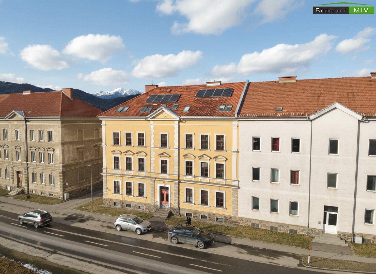 Historisches Gebäude mit gelber Fassade und Solarpaneelen auf dem Dach unter blauem Himmel.