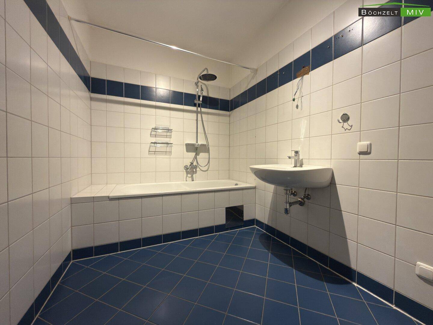 Badezimmer mit Badewanne, Dusche und Waschbecken, gefliest in Blau und Weiß.