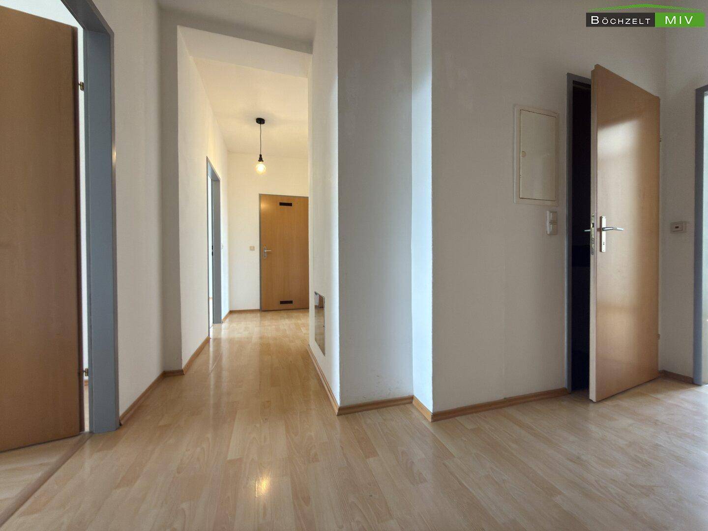 Heller Flur einer Wohnung mit Laminatboden und Holztüren, der zu weiteren Räumen führt.